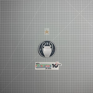 Peut inclure: Plusieurs écussons sur fond quadrillé gris. L'un représente le trophée de la Ligue des Champions de l'UEFA. Un autre affiche le texte "UEFA FOUNDATION for children 10 YEARS". Une étoile dorée est également présente.