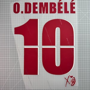 Peut inclure: Une feuille de vinyle thermocollant rouge avec le nom "O. DEMBÉLÉ" et le numéro "10" imprimés. Le numéro 10 est grand et en gras. Un petit graphique est dans le coin inférieur droit. La feuille est sur une grille grise.
