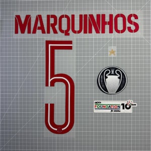 Peut inclure: Transfert thermique rouge pour un maillot, avec le nom "MARQUINHOS" au-dessus du numéro "5". Comprend un écusson de la Ligue des Champions de l'UEFA, une étoile dorée et un écusson "UEFA Foundation for children 10 years".