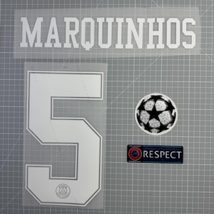 Peut inclure: Éléments en vinyle thermocollant blanc pour un maillot de football, comprenant le nom "MARQUINHOS", le numéro "5", un graphisme de ballon de football et un écusson "RESPECT". Les éléments sont sur un fond quadrillé gris.