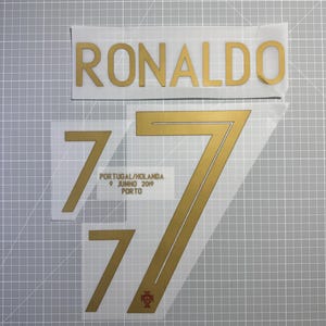 Peut inclure: Vinyle thermocollant doré pour maillot, avec le nom "RONALDO" et le numéro "7". Comprend le chiffre 7 plus petit et le texte "PORTUGAL/HOLANDA 9 JUNHO 2019 PORTO" avec un écusson portugais.