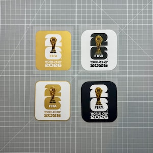 Peut inclure: Quatre autocollants carrés présentant le logo de la Coupe du Monde de la FIFA 2026. Le design comprend un grand nombre 26 avec un trophée doré remplaçant le zéro, et le texte FIFA WORLD CUP 2026. Les couleurs incluent or sur blanc, noir sur blanc, blanc sur or et blanc sur noir.