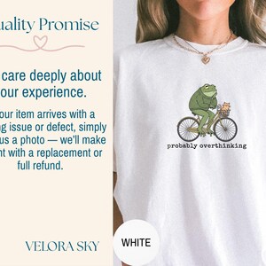 May include: White t-shirt featuring a green frog riding a bicycle with a small cat in the basket. The text "probably overthinking" is printed below the graphic. The shirt also has the text "Quality Promise" and "We care deeply about your experience."