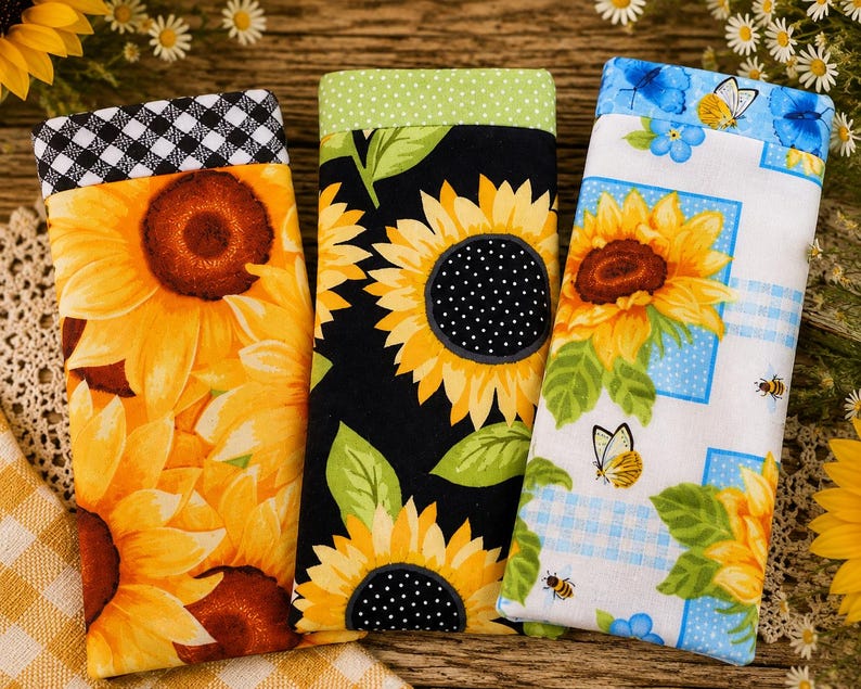 May include: Three rectangular fabric cases for eyeglasses or small items. The left case features yellow sunflowers with a black and white gingham top. The center case has yellow sunflowers on black with a green polka dot top. The right case displays sunflowers, butterflies, and bees on white.