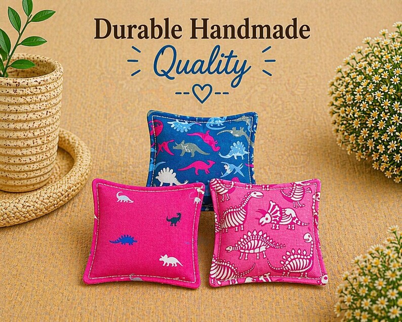 May include: Three small square fabric cushions featuring dinosaur patterns. One cushion is blue with multi-colored dinosaurs, while two are pink with white dinosaur silhouettes and skeletal prints. Text above reads Durable Handmade Quality.