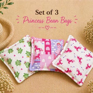 May include: A set of three square bean bags featuring fabric prints of green frogs with crowns, a pink castle with a princess and unicorns, and pink unicorns with stars. The text Set of 3 Princess Bean Bags is printed above the items.