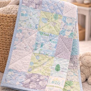 May include: A patchwork baby quilt with a light blue border. The quilt features squares with sheep, trees, and text that reads "Lamb", "Hugs", and "Big". The color palette includes blue, green, and lavender.