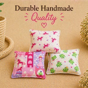 May include: Three small square fabric pillows featuring colorful prints. One pillow has pink unicorns, another displays a pink castle with a princess and frog, and the third features green frogs. Text reads Durable Handmade Quality.