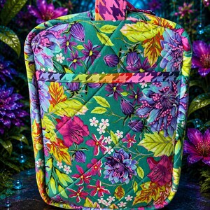 May include: A quilted fabric bag featuring a vibrant floral pattern on a green background. The design includes purple, pink, and yellow flowers with green leaves. A horizontal band with a multicolored houndstooth pattern accents the front.