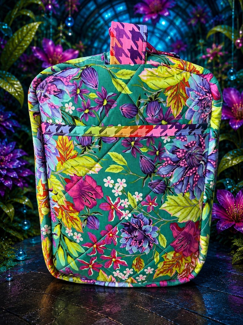 May include: A quilted fabric bag featuring a vibrant floral pattern on a green background. The design includes purple, pink, and yellow flowers with green leaves. A horizontal band with a multicolored houndstooth pattern accents the front.