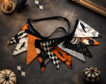 May include: A fabric bunting banner featuring triangular flags with various patterns including black crows, orange pumpkins, and black and white checkered designs. The flags are connected by a black ribbon, creating a decorative hanging garland.