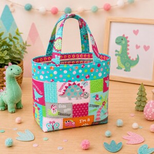 May include: A fabric tote bag featuring a patchwork design with various dinosaur illustrations, polka dots, and floral patterns in bright shades of turquoise, pink, orange, and green. The bag has two matching fabric handles and a rectangular base.