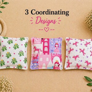 May include: Three square fabric pouches with the text 3 Coordinating Designs. The left pouch features green frogs with crowns and pink hearts. The center pouch shows a pink castle, a princess, and a unicorn. The right pouch displays pink unicorns.