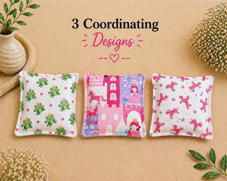 May include: Three square fabric pouches with the text 3 Coordinating Designs. The left pouch features green frogs with crowns and pink hearts. The center pouch shows a pink castle, a princess, and a unicorn. The right pouch displays pink unicorns.