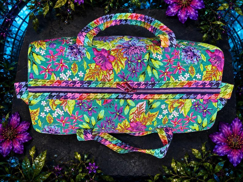 May include: A rectangular fabric bag featuring a vibrant floral pattern in shades of teal, magenta, purple, and yellow. The bag includes a top zipper closure and two handles, both decorated with a multi-colored houndstooth pattern in rainbow hues.