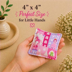 May include: A square fabric bean bag measuring 4 inches by 4 inches, featuring a pink and purple pattern with a unicorn, a castle, a princess, and a frog. The text 4 x 4 Perfect Size for Little Hands is printed above the object.