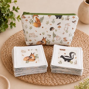 May include: A zippered pouch with a white background featuring a woodland animal print including foxes, rabbits, and mushrooms, paired with two stacks of square fabric coasters, one stack showing a fawn and the other showing a skunk illustration.