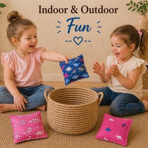 May include: A set of three square fabric bean bags featuring dinosaur patterns in blue and pink, accompanied by a round woven jute basket. The text "Indoor & Outdoor Fun" is displayed above the items in a decorative font style.