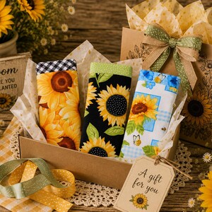May include: Three rectangular fabric cases featuring sunflower patterns are nestled in a brown gift box. One case has a black and white gingham top, one has a green dotted top, and one has a blue patterned top. A gift tag reads A gift for you.