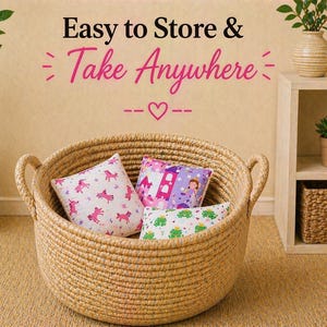 May include: A round, tan woven rope basket with two side handles containing three small square pillows. The pillows feature prints of pink unicorns, a purple castle with a princess, and green frogs. Text above reads: Easy to Store & Take Anywhere.
