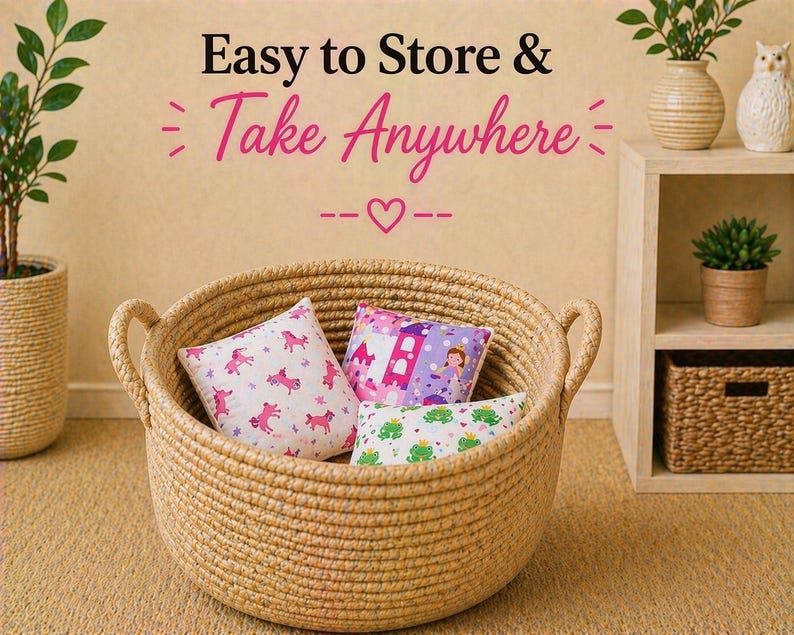 May include: A round, tan woven rope basket with two side handles containing three small square pillows. The pillows feature prints of pink unicorns, a purple castle with a princess, and green frogs. Text above reads: Easy to Store & Take Anywhere.
