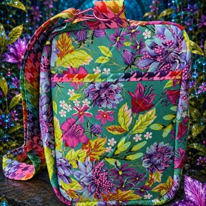 May include: A quilted rectangular crossbody bag featuring a vibrant floral pattern in shades of teal, purple, pink, and yellow. The bag includes a matching adjustable strap with a colorful houndstooth print and a pink metal swivel clasp.