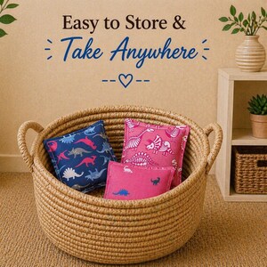 May include: A round, woven rope basket with two handles containing three small, square fabric pillows featuring dinosaur patterns in blue and pink. The text above the basket reads Easy to Store & Take Anywhere with a heart symbol.