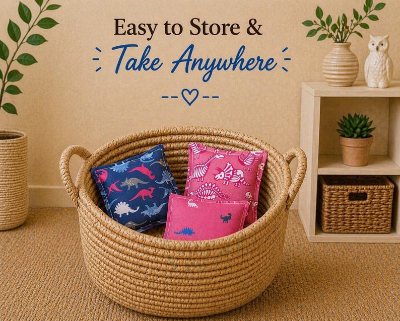 May include: A round, woven rope basket with two handles containing three small, square fabric pillows featuring dinosaur patterns in blue and pink. The text above the basket reads Easy to Store & Take Anywhere with a heart symbol.
