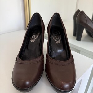 Op de afbeelding: Een paar bruine leren pumps met een ronde neus en een blokhak. De schoenen hebben de merknaam "TOD'S" op de binnenzool gedrukt. De hakken zijn ongeveer 7.6 cm hoog.