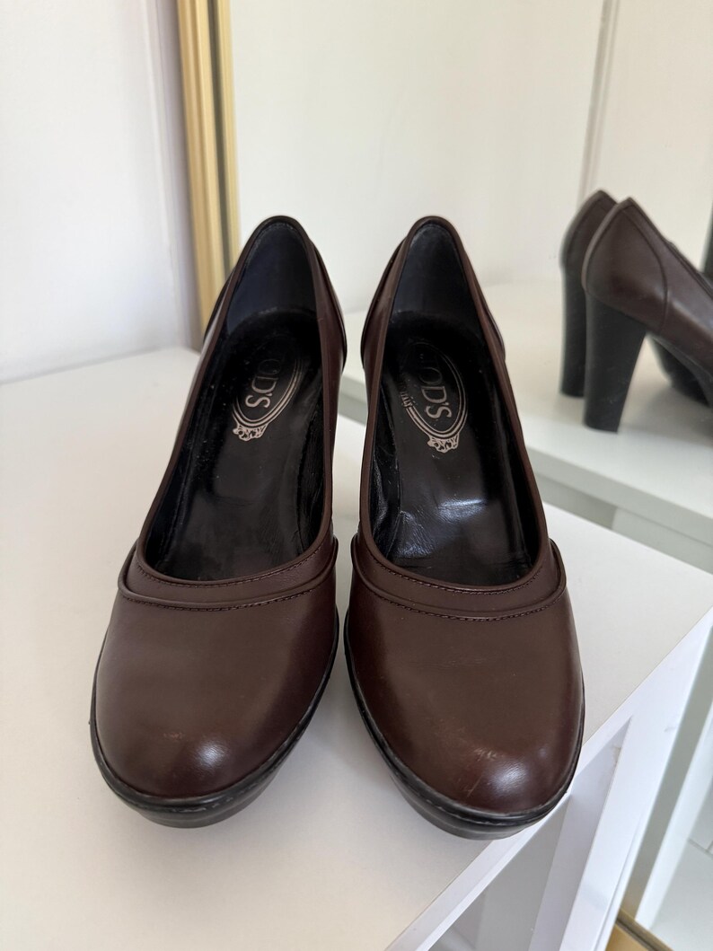 Op de afbeelding: Een paar bruine leren pumps met een ronde neus en een blokhak. De schoenen hebben de merknaam "TOD'S" op de binnenzool gedrukt. De hakken zijn ongeveer 7.6 cm hoog.