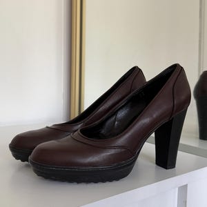 Op de afbeelding: Een paar bruine leren plateau pumps met zwarte blokhakken. De schoenen hebben een ronde neus en een plateauzool. De hakken zijn ongeveer 10 cm hoog.