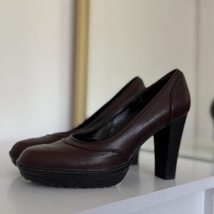 Op de afbeelding: Een paar bruine leren plateau pumps met zwarte blokhakken. De schoenen hebben een ronde neus en een plateauzool. De hakken zijn ongeveer 7,6 cm hoog.