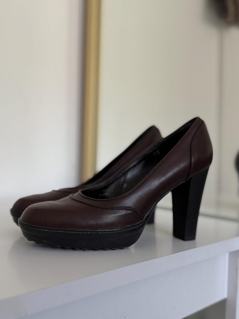 Op de afbeelding: Een paar bruine leren plateau pumps met zwarte blokhakken. De schoenen hebben een ronde neus en een plateauzool. De hakken zijn ongeveer 7,6 cm hoog.