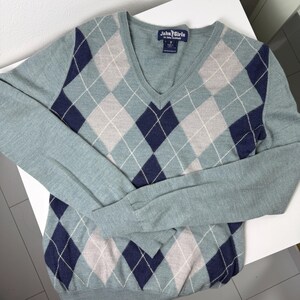 May include: A pale blue V-neck sweater featuring a navy, grey, and white argyle design. The long-sleeved jumper has a label that says "John Girls".