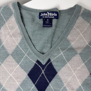 May include: A teal V-neck sweater featuring a traditional argyle design in grey and navy. The label reads "John Girls by John Ashfield" and "Made in Italy". The sweater is a size small. The argyle pattern is made of diamonds.
