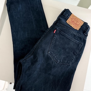 Può includere: Jeans in denim blu scuro con un classico design a cinque tasche. I jeans presentano un'etichetta rossa Levi's sulla tasca posteriore e una toppa in pelle marrone. I jeans sono un modello a gamba dritta.