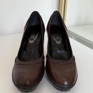 Op de afbeelding: Een paar bruine leren pumps met een ronde neus en een blokhak. De schoenen hebben de merknaam "TOD'S" in reli&euml;f op de binnenzool. De hakken zijn ongeveer 7.6 cm hoog.