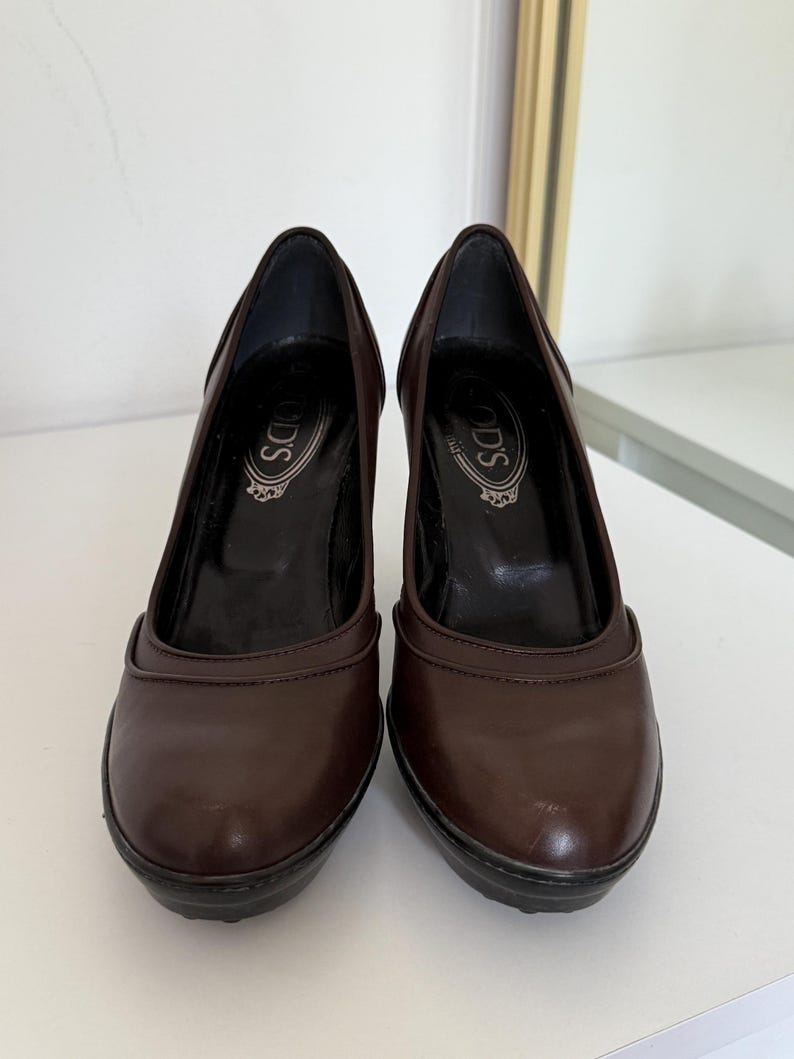 Op de afbeelding: Een paar bruine leren pumps met een ronde neus en een blokhak. De schoenen hebben de merknaam "TOD'S" in reli&euml;f op de binnenzool. De hakken zijn ongeveer 7.6 cm hoog.
