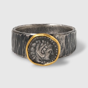 May include: A silver ring with a textured band and a gold-rimmed coin featuring a profile of a person's head.