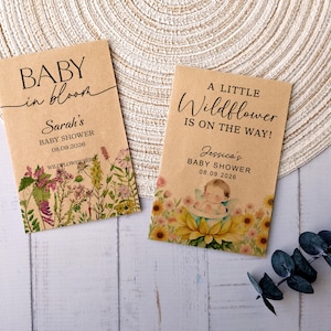 May include: Two kraft paper seed packets for a baby shower. One reads "BABY in bloom" and "Sarah's BABY SHOWER 08.09.2026". The other says "A LITTLE Wildflower IS ON THE WAY!" and "Jessica's BABY SHOWER 08.09.2026". Both have floral illustrations.