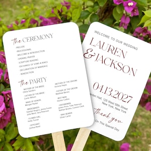 May include: Two white wedding program fans with rounded corners and wooden handles. One side displays the ceremony order and wedding party list. The other side features the names Lauren and Jackson, the date 04.13.2027, and the location details.