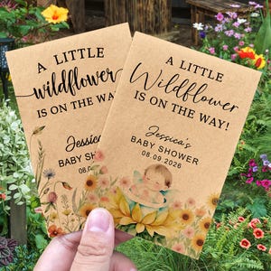 May include: Two kraft paper baby shower announcements with floral illustrations and the text "A Little Wildflower Is On The Way!". The announcements include the name "Jessica's" and the date "08.09.2026".