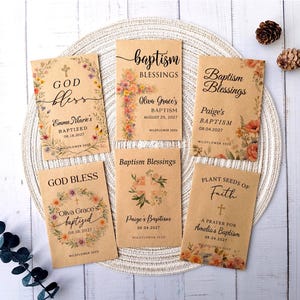 May include: A collection of kraft paper seed packets with floral designs and text. The packets read "God Bless," "Baptism Blessings," and "Plant Seeds of Faith." Each packet includes names and baptism dates.