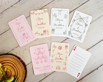May include: A collection of wedding-themed cards with various designs and the names "Claire & Jonathan" and the date "02.06.2026". The cards feature illustrations of champagne glasses, cakes, and other celebratory elements. The Ace of Hearts playing card is also visible.