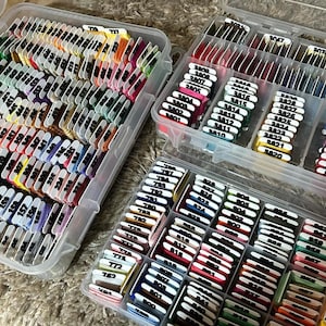 May include: Two clear plastic storage containers filled with colorful embroidery floss spools. The spools are labeled with numbers.