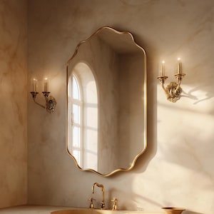 May include: A gold-framed mirror with a scalloped edge hangs above a marble countertop. Two sconces with lit candles flank the mirror. A gold faucet and sink are visible, creating a luxurious bathroom aesthetic.