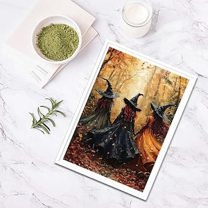May include: A framed art print depicting three figures wearing pointed hats and long cloaks walking through an autumn forest with golden leaves. The print is displayed alongside a small white bowl of green powder and a sprig of rosemary.