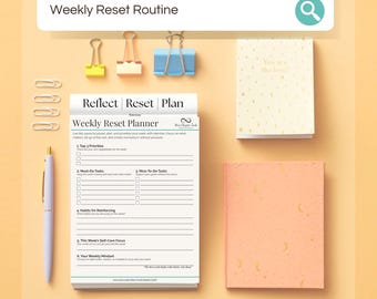May include: A weekly reset planner with a pen, paperclips, and stationery. The planner is open to a page with prompts for priorities, tasks, and self-care. A small notebook with gold accents and a peach-colored notebook are also present.