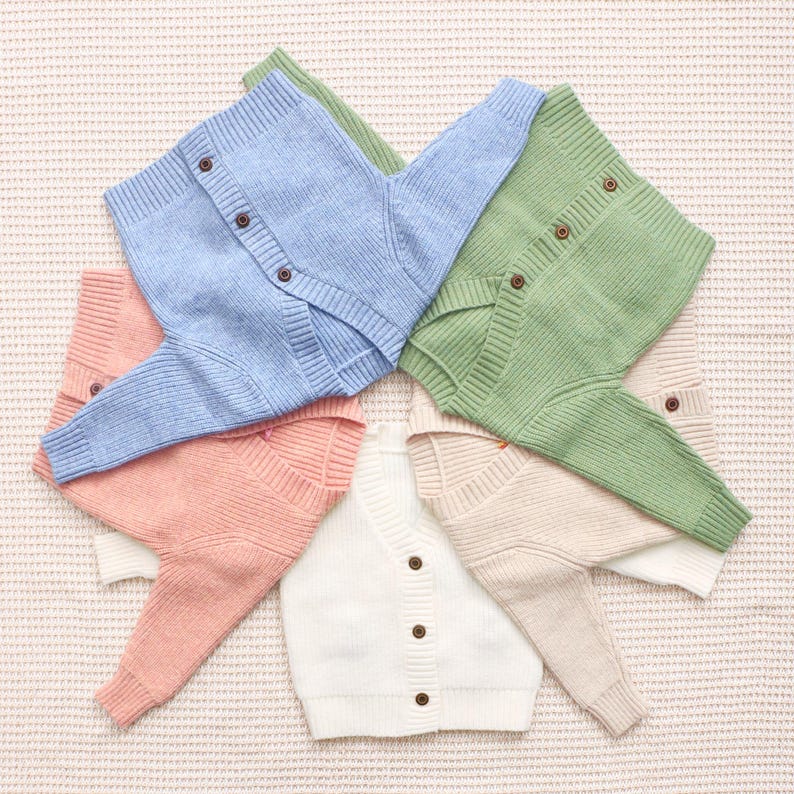Peut inclure: Plusieurs cardigans boutonn&eacute;s de couleurs pastel sont pr&eacute;sent&eacute;s. Les couleurs incluent le bleu clair, le rose, le vert et le blanc. Les cardigans sont en maille c&ocirc;tel&eacute;e et ont des boutons marron.