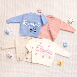 Peut inclure: Quatre cardigans en tricot de couleurs pastel. Un cardigan bleu clair avec le nom "Rupert" brod&eacute; en blanc et un motif de voiture. Un cardigan rose, un cardigan cr&egrave;me et un cardigan blanc avec le nom "Elodie" brod&eacute; en rose avec des motifs floraux.